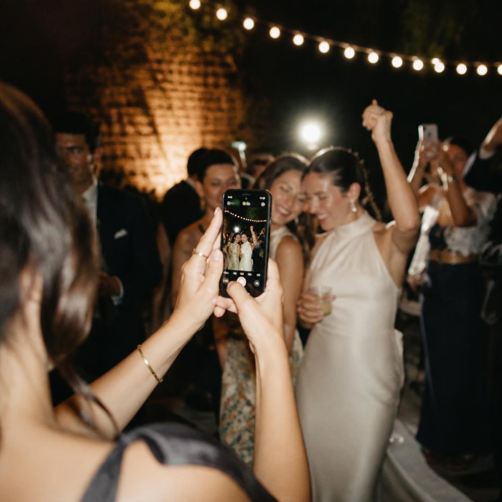 A guest taking a phone photo of friends dancing at a wedding